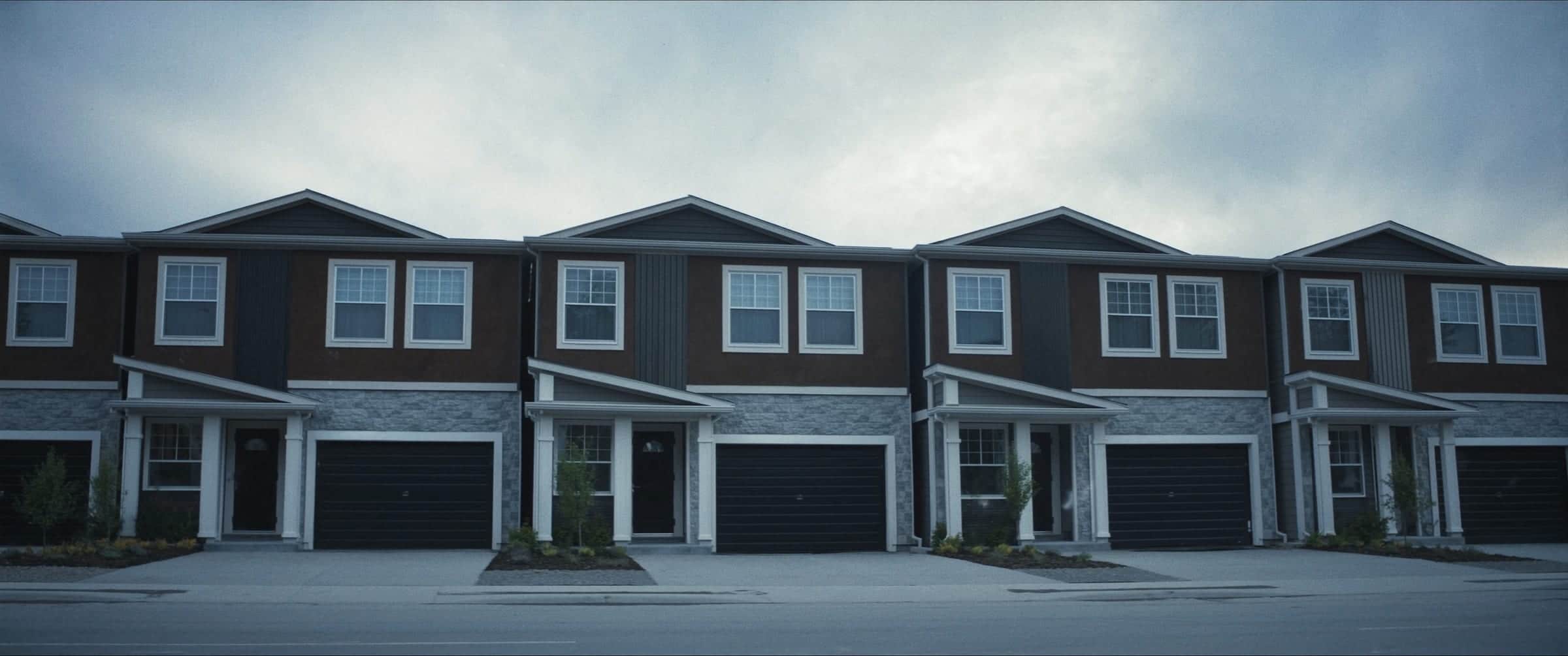 A row of newly completed townhomes seen straight on, repeating bays of dark cladding and pale trim under an overcast sky.
